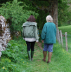 Two people walking down a norrow lane between trees.